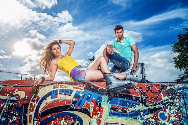 Chica en patines yace en la pared con graffiti junto con un chico