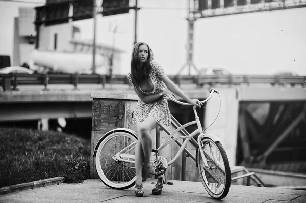 Foto en estilo retro, una chica con un vestido corto con una bicicleta en el fondo de un cruce de carreteras