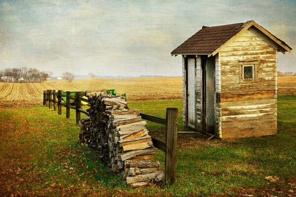 A shabby building in the middle of a field with firewood