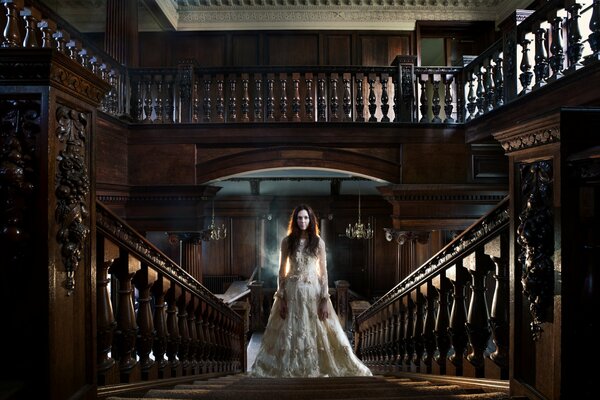 A girl in a white dress on the stairs in an old house