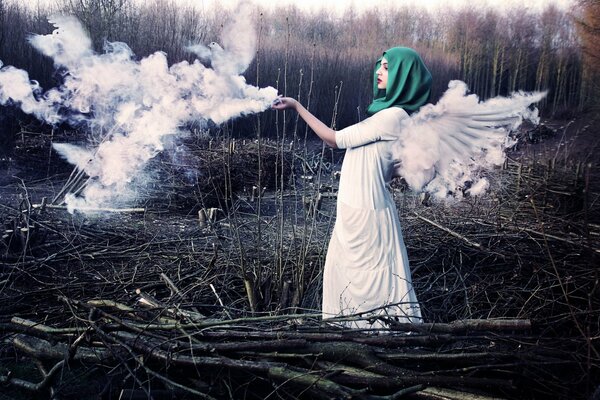 La jeune fille dans une robe blanche simple avec des ailes et dans un foulard vert se tient dans une clairière avec des brindilles