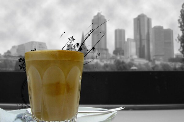 A glass cup with an orange drink on a white plate on a black and white background of the city