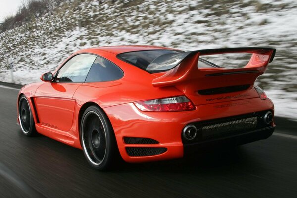 Un coche rojo conduce a lo largo de una carretera cubierta de nieve