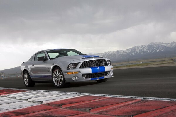 Shelby s racing car rushes at speed along the track against the backdrop of mountains