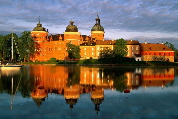 Schönes rotes Schloss reflektiert im Wasser mit einer kleinen Yacht