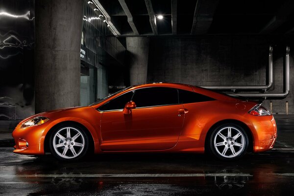 Orange Mitsubishi in an underground parking lot with a metal wall