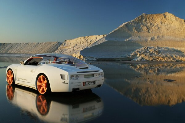 Un auto sportiva bianca si trova su ghiaccio sciolto contro una collina di neve e ghiaccio