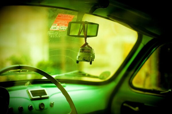 A green retro car with a toy copy of itself on the mirror