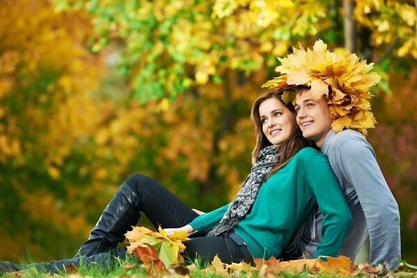 Una joven pareja en el bosque de otoño con una corona de hojas de arce