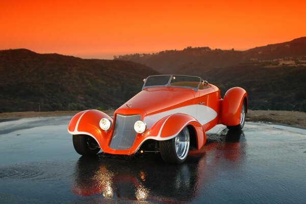 L Hot Rod arancione si trova sull asfaltata bagnata contro le colline e il tramonto