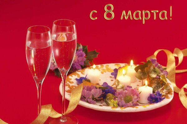 On a red background there are two glasses of champagne, next to a plate with flowers and candles