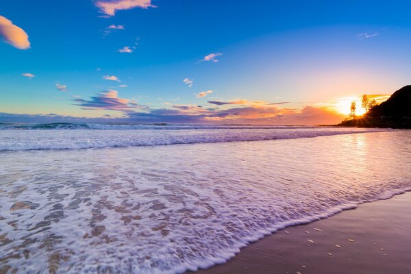 Foam wave rolling on the sea sand at sunset