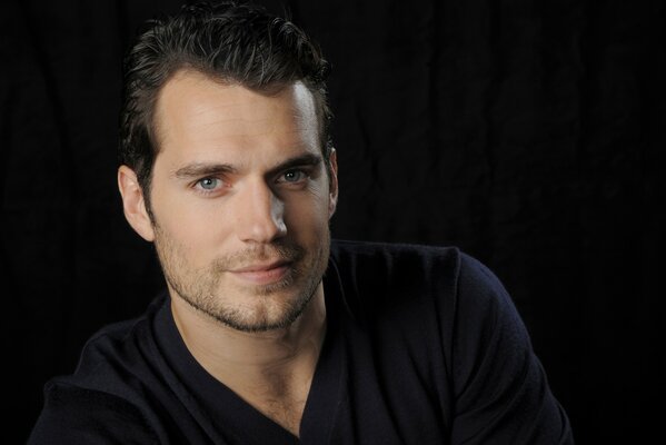 Henry Cavill on a black background looks into the lens and smiles