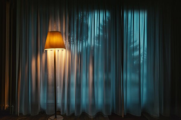 A lamp in a dark room with blue curtains