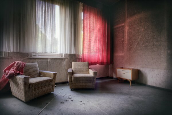 Sillones blancos en el piso de concreto contra una ventana con una cortina roja