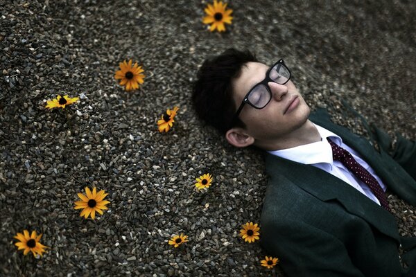 Homme en costume se trouve sur les pierres avec des fleurs