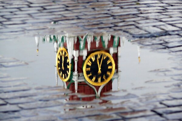 Reflection of the clock on the Kremlin towers in a puddle