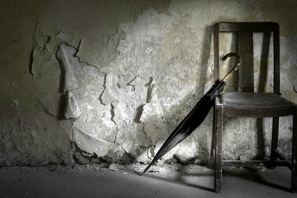 An umbrella leaning against a chair against a peeling wall