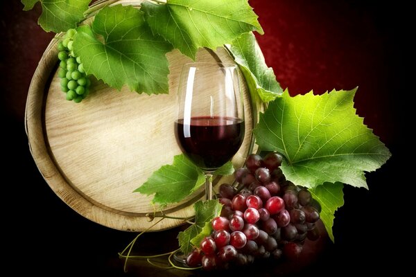 A glass of wine on the background of a barrel and grapes