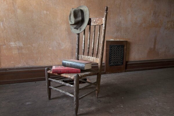 A stack of books lies on an antique chair with a hat