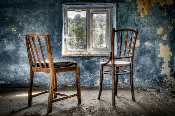 Two chairs near the window with cobwebs in an abandoned room