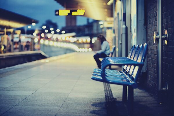 The girl is sitting on a chair in the evening at the city train station