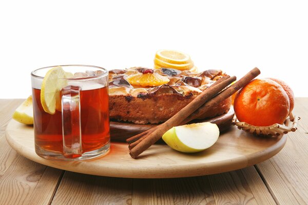 Tasse Tee, Kuchen, Zimtstangen, Äpfel und Orangen auf einem Tablett