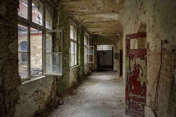 A ruined corridor with broken windows and stripped doors