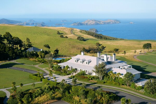 White mansion on a green hill with trees near the sea