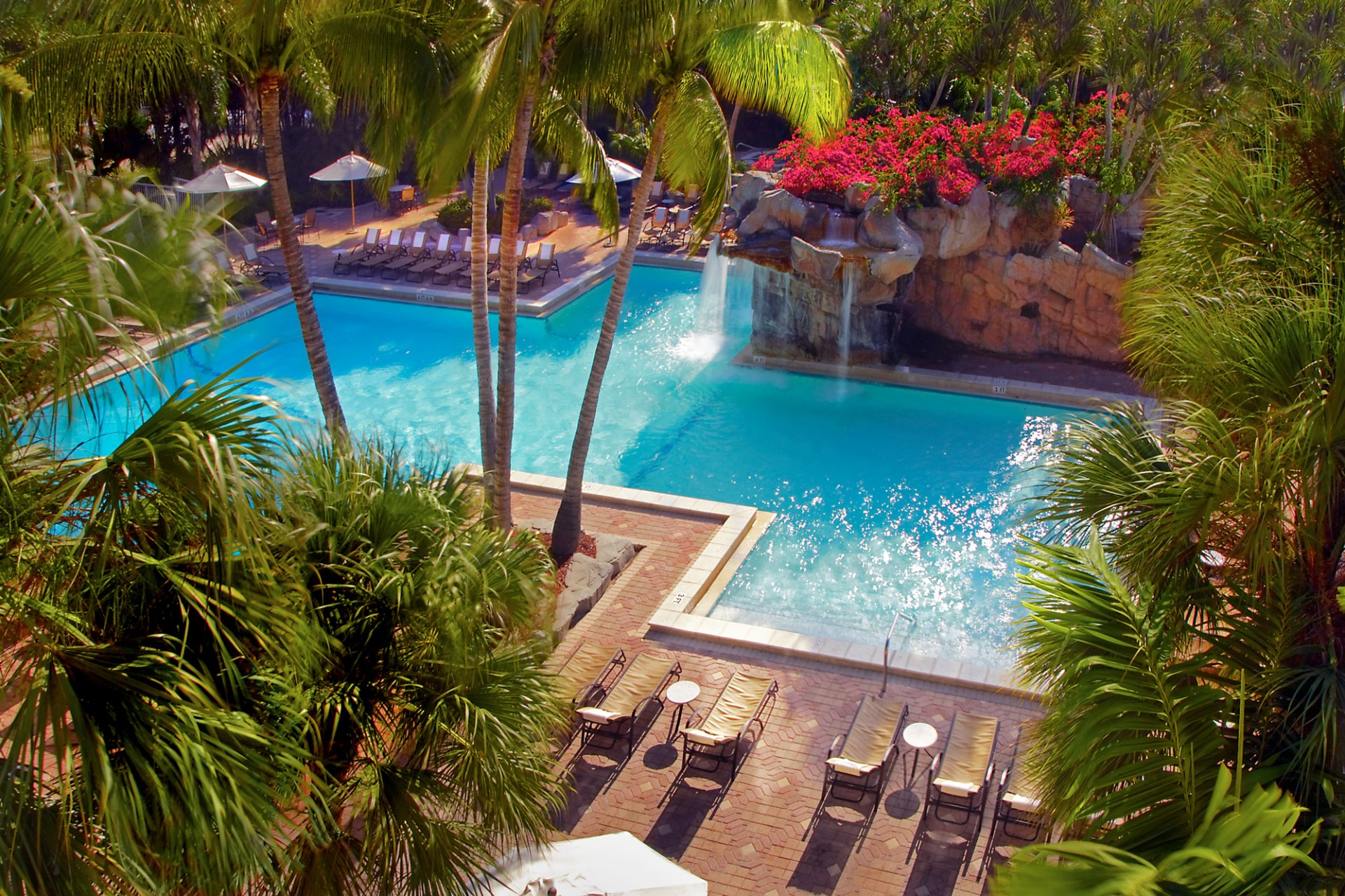 pool wasserfall steine palmen blumen sonnenliegen