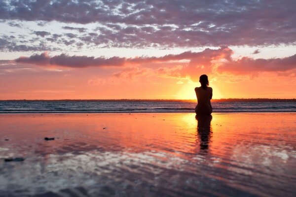 A girl on the shore looks at the setting sun