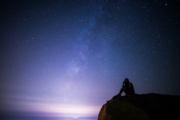 Ragazza sulla roccia di notte sullo sfondo del cielo stellato