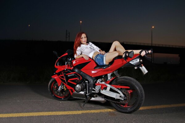 A beautiful red-haired girl is lying on a motorcycle