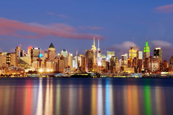 At night , the lights of New York are reflected in the water