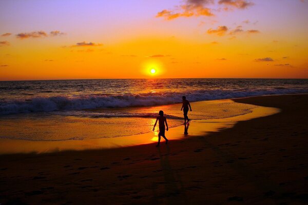 Les gens se promènent sur la plage au coucher du soleil