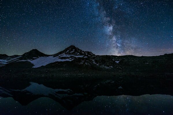 Reflexion der Sterne in einem Nachtsee mit schneebedeckten Bergen