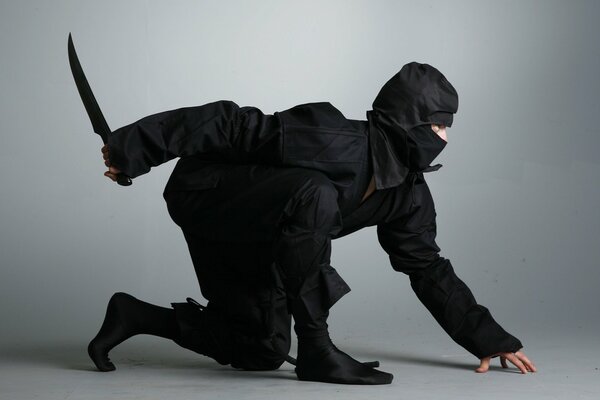 A ninja in a black suit with a dagger hid in an ambush, ready to strike