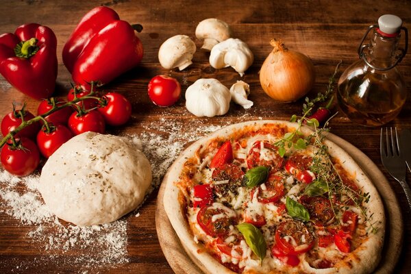 Pizza con tomates y pimientos. En la mesa de masa y verduras
