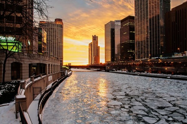 Hielo agrietado en el río en los rayos del atardecer de la ciudad