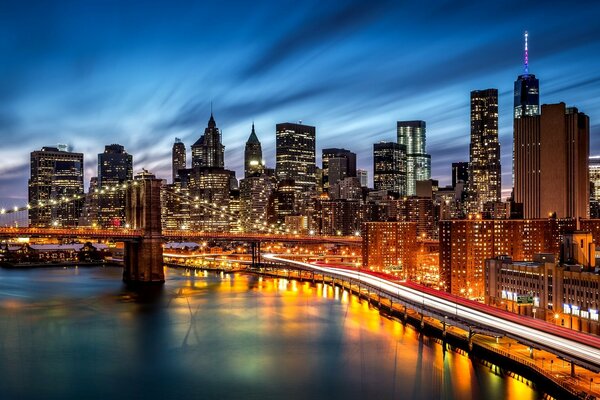 The night lights of New York. View of the Brooklyn Bridge and illuminated skyscrapers. Big City Lights