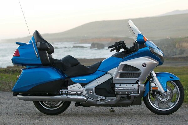 A blue motorcycle stands against the background of a lake and mountains