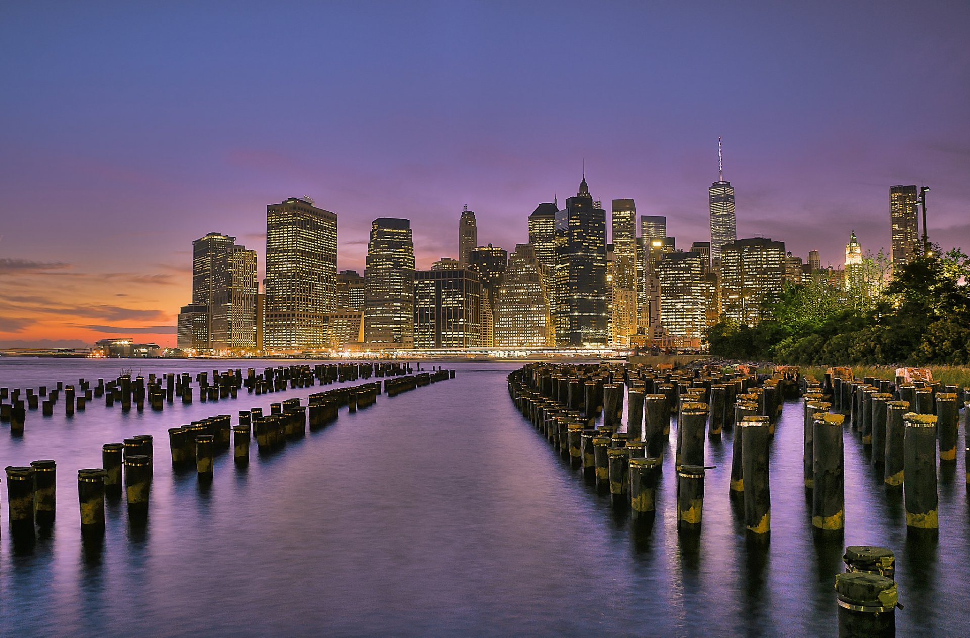 new york usa brooklyn bridge park lower manhattan east river city lights skyscrapers buildings river pillars shore evening sunset orange purple sky