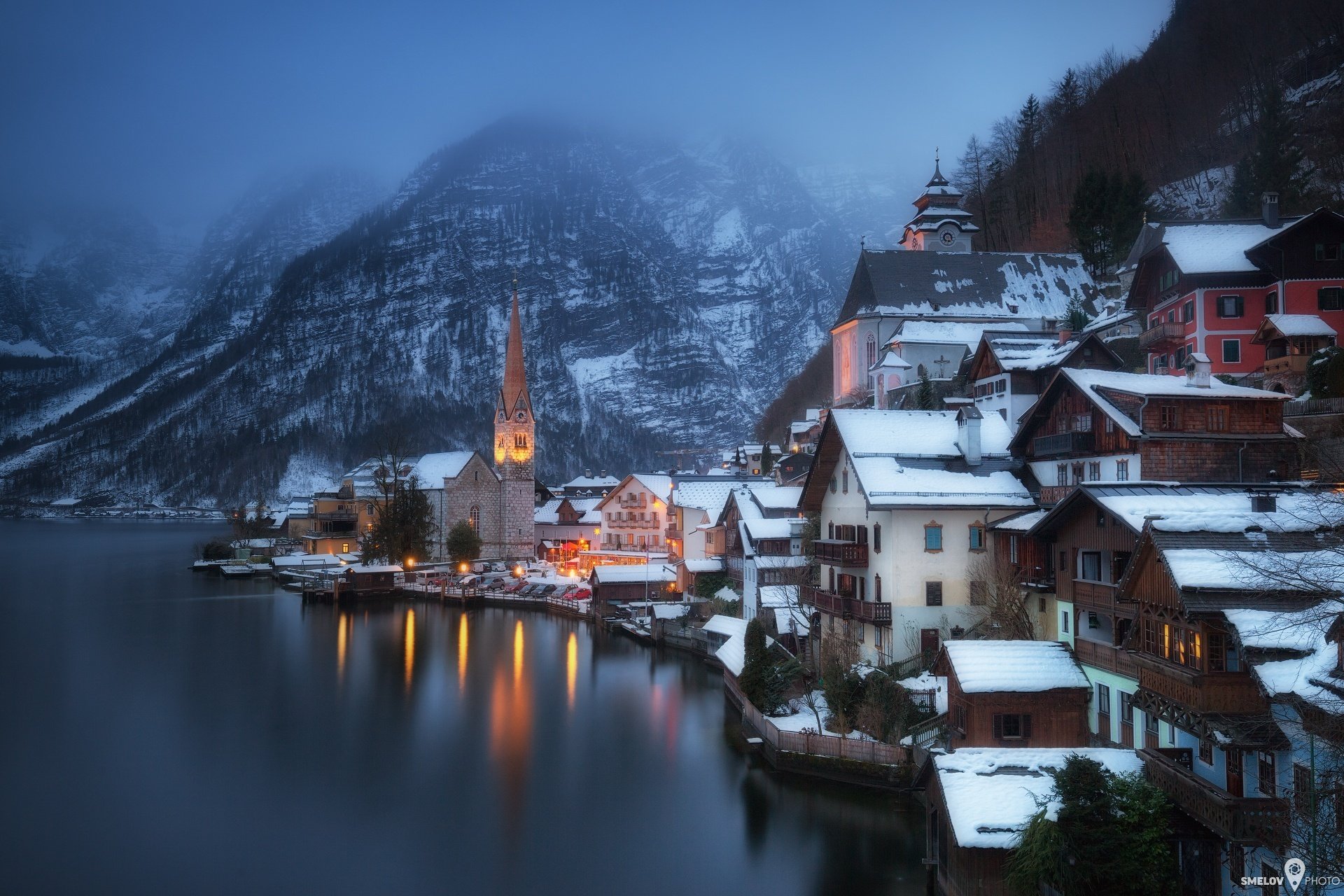 austria town commune hallstatt salzkammergut winter snow mountain alps lake beach house lights haze