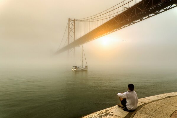 Ein Mann schaut auf den Sonnenaufgang über Nebel und Brücke