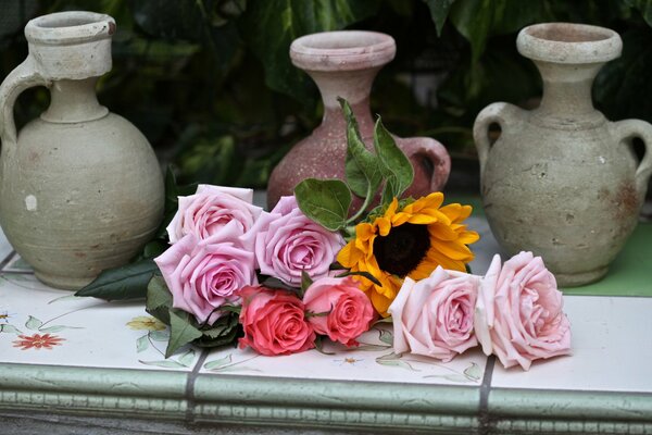 Pink roses and sunflower on the background of vases