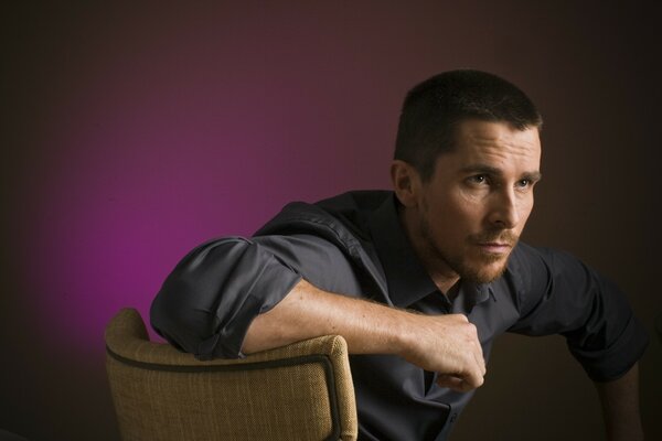 Christian Bale the actor in the photo is sitting on a chair