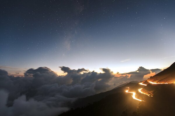 Cielo al atardecer con nubes bajas y camino en la colina con luces