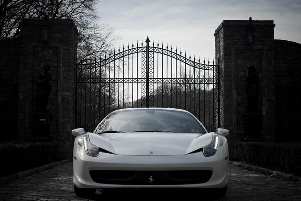 Une Ferrari blanche se tient devant une porte en fer forgé