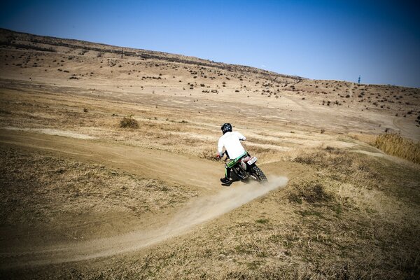 A motorcyclist on a motorcycle rushes through fields and forests probably to his madam from a neighboring village