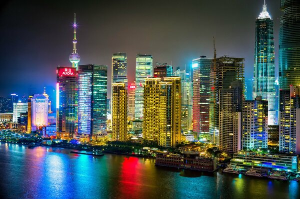 The night city of Shanghai burns with lights and is reflected in the river